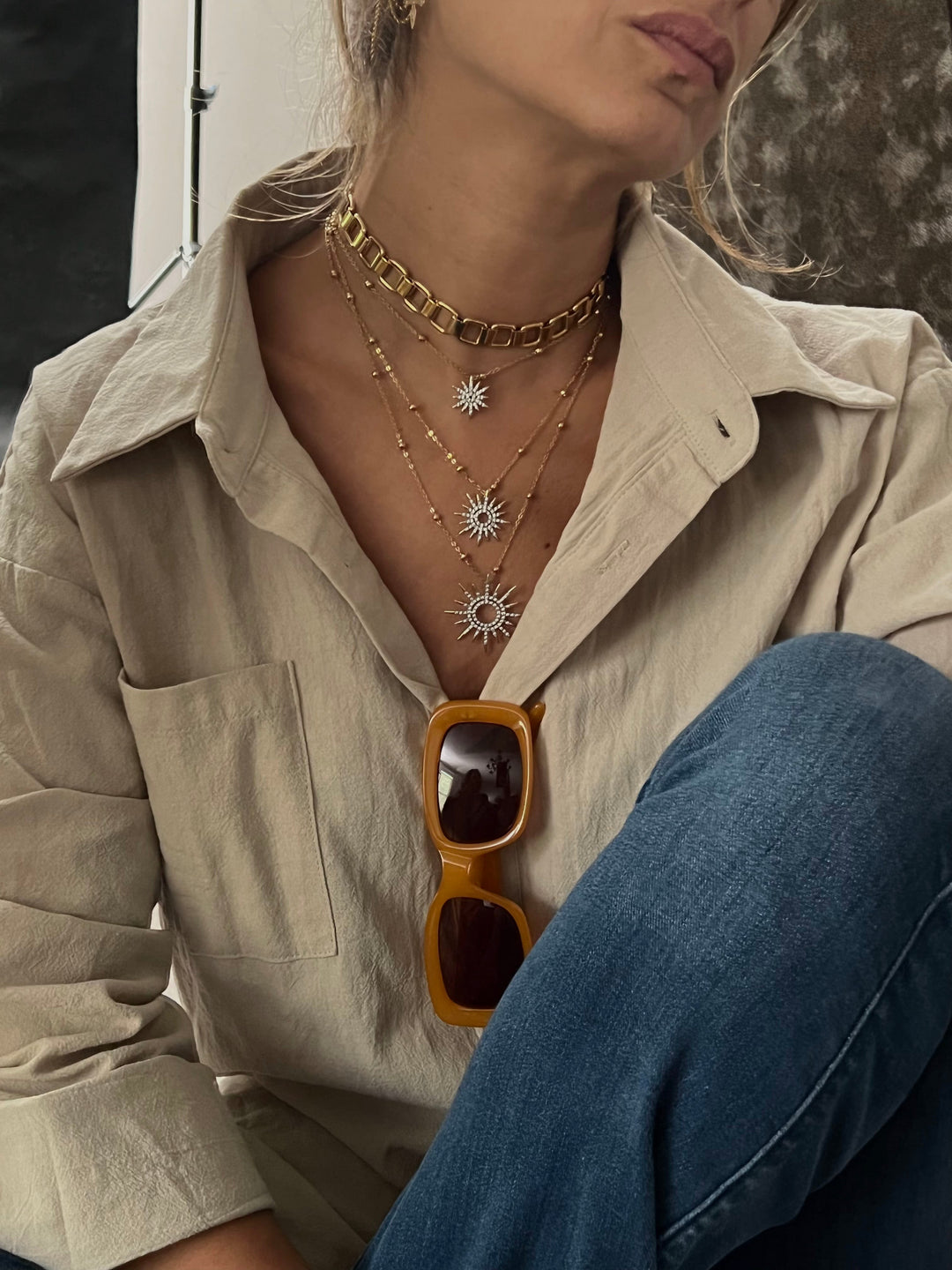 Woman wearing a button-up blouse and a layered necklace with 3 suns or stars